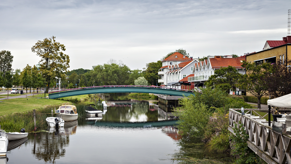 Image of the riverfront in Kungsbacka, outside of Gothenburg Sweden. A bridge crossing a small river with a few boats docked by the side.  Houses on the right of the bridge and a road to the left.